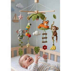 Op de afbeelding: Handgemaakte gehaakte baby mobile met jungle dieren. De mobile bevat een tijger, aap, papegaai, olifant, wolken, sterren en bladeren, allemaal opgehangen aan een houten frame. De baby ligt in een bed en kijkt naar de mobile.