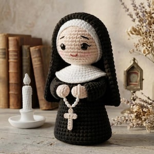 Puede incluir: Muñeca de ganchillo hecha a mano de una monja, vestida con un hábito negro con una toca y un cuello blancos. La muñeca tiene una cara sonriente y sostiene un rosario con una cruz. Una vela blanca y libros antiguos están en el fondo.