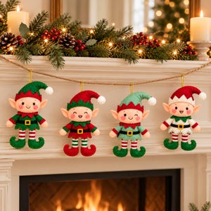May include: Four felt elf ornaments hanging from a rustic twine string. Each elf features a pointed hat, a smiling face with rosy cheeks, and a belt with a gold buckle. The elves wear outfits in combinations of red, green, white, and black felt.