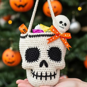 May include: A crocheted skull-shaped bag with black eyes, nose, and mouth details. The bag has a white handle and is filled with colorful candies. An orange polka-dot bow and a small skull adorn the top. Halloween-themed.