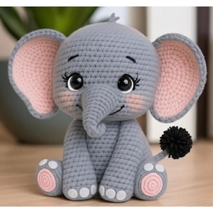 Può includere: Un elefante all'uncinetto grigio fatto a mano con interno orecchie e cuscinetti dei piedi rosa. L'elefante ha grandi occhi espressivi, una proboscide e una piccola coda a pompon nera. È seduto su una superficie di legno.