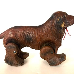 May include: A brown wooden toy dog with a red string attached to its neck. The dog has four wheels and is a vintage toy.