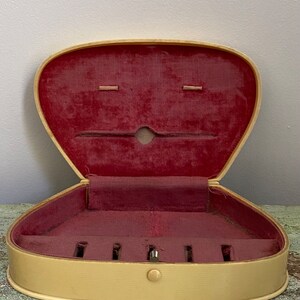 May include: A heart-shaped, cream-colored jewelry box with a red velvet interior. The box has a hinged lid and a small button closure. The interior has several compartments for storing jewelry.