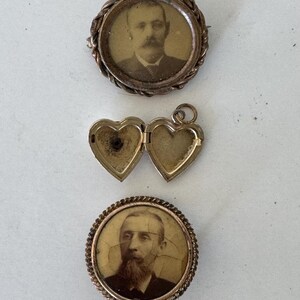 May include: Three antique gold-toned locket pendants. Two of the lockets feature a circular frame with a black and white photograph of a man inside. The third locket is heart-shaped and open.