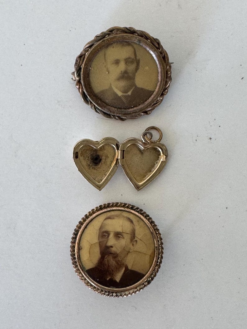 May include: Three antique gold-toned locket pendants. Two of the lockets feature a circular frame with a black and white photograph of a man inside. The third locket is heart-shaped and open.