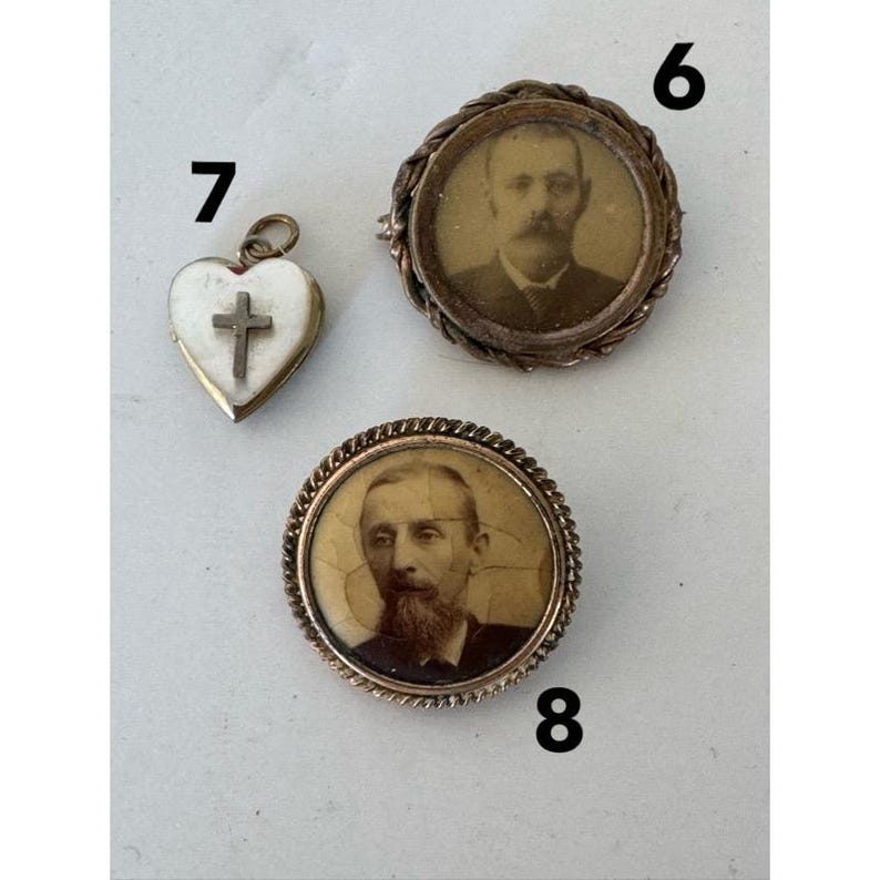 May include: Three antique gold-toned brooches with portraits. One brooch features a heart-shaped locket with a cross inside. Another brooch features a round portrait of a man with a mustache and beard. The third brooch features a round portrait of a man with a beard.