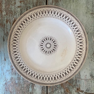 May include: A white ceramic plate with a brown and white geometric pattern around the edge. The center of the plate has a smaller, similar pattern.