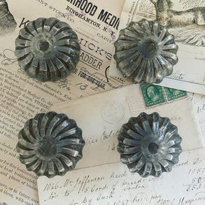 May include: Four antique silver-toned metal knobs with a swirl design. The knobs have a raised center and are slightly worn.