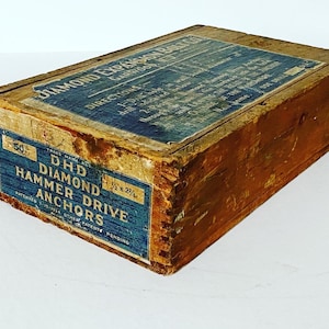 May include: A vintage wooden box with blue and white labels. The labels read "DIAMOND EXPANSION BOLT CO" and "DHD DIAMOND HAMMER DRIVE ANCHORS". The box is weathered, showing signs of age and use. The dimensions are 1 1/2 x 2 1/4 inches.