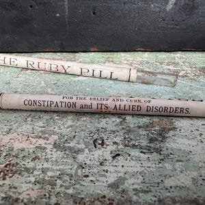 May include: Two vintage glass tubes with paper labels. One reads "THE RUBY PILL" and the other states "FOR THE RELIEF AND CURE OF CONSTIPATION and ITS ALLIED DISORDERS."