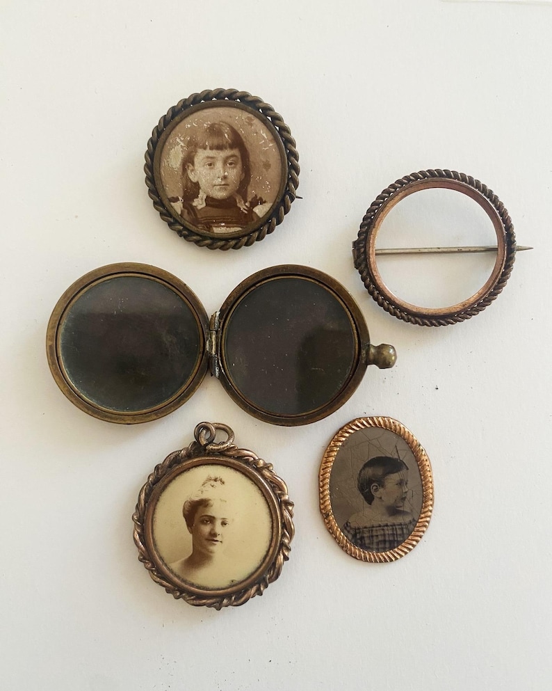 May include: Five antique locket style brooches with ornate gold frames. Each locket features a black and white photograph of a person. Two of the lockets are round, two are oval, and one is a simple circle.