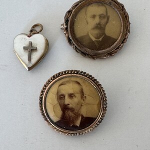 May include: Three antique gold-toned brooches. Two of the brooches feature a portrait of a man in a round frame. The third brooch is a heart-shaped locket with a white cross.