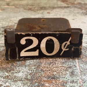 May include: A vintage metal price tag with black paint and white lettering. The tag reads "20&cent;".