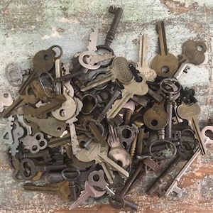 May include: A large pile of vintage keys in various sizes and styles, including skeleton keys, ornate keys, and keys with decorative handles. The keys are made of brass and steel and have a patina finish. Some of the keys have the word "Miller" engraved on them.