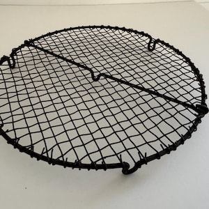 May include: A round black wire cooling rack with a criss-cross pattern. The rack has four legs and is made of metal.