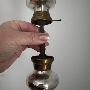 May include: Antique door knob with a mirrored glass bulbous shape and brass accents. The knob has a long, dark metal stem and a small, cylindrical pin. The glass reflects the surrounding environment.