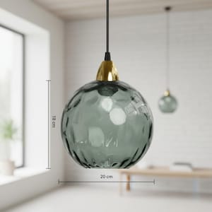 May include: A hanging pendant light with a textured, smoky gray glass globe, 7 inches in diameter and 7 inches tall, suspended from a black cord. The fixture has a gold-colored metal cap. Another similar light is visible in the background.