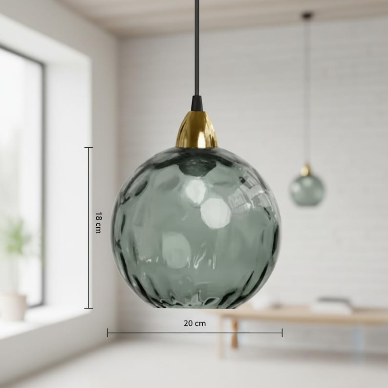 May include: A hanging pendant light with a textured, smoky gray glass globe, 7 inches in diameter and 7 inches tall, suspended from a black cord. The fixture has a gold-colored metal cap. Another similar light is visible in the background.