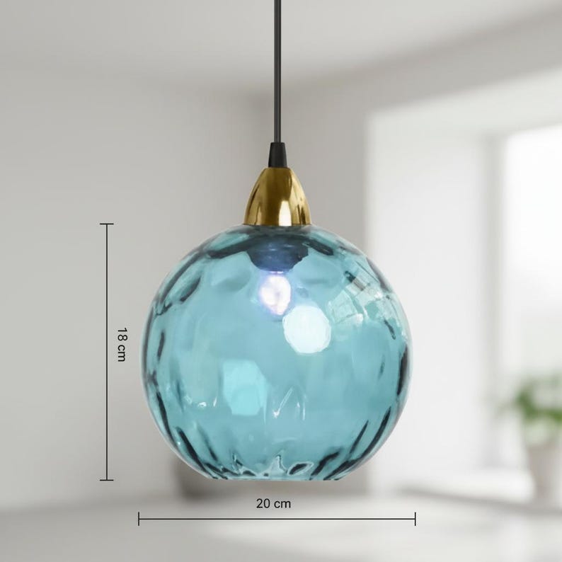 May include: A blue glass pendant light with a textured surface, measuring 7 inches in height and 8 inches in diameter. The light fixture has a gold-colored cap and a black cord. The light is hanging in front of a white background.
