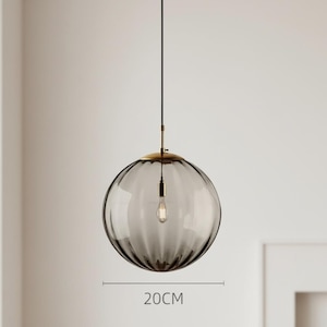 May include: A gray glass pendant light with a ribbed design, measuring approximately 7.9 inches in diameter. The light fixture has a brass-colored top and a black cord. The bulb is visible inside the glass sphere.
