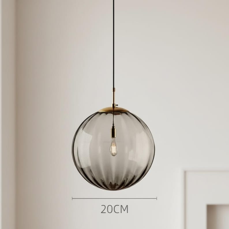 May include: A gray glass pendant light with a ribbed design, measuring approximately 7.9 inches in diameter. The light fixture has a brass-colored top and a black cord. The bulb is visible inside the glass sphere.