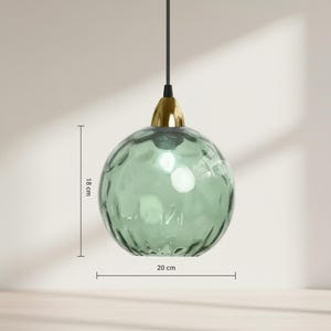 May include: A hanging, spherical pendant light with a textured, seafoam green glass shade. The light fixture is 7 inches in diameter and 7 inches tall, with a gold-colored metal cap and a black cord.