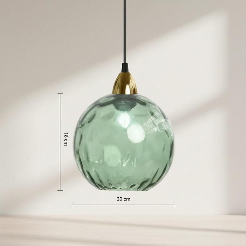 May include: A hanging, spherical pendant light with a textured, seafoam green glass shade. The light fixture is 7 inches in diameter and 7 inches tall, with a gold-colored metal cap and a black cord.