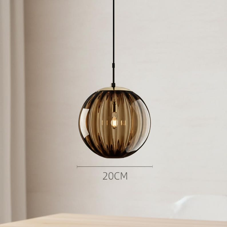 May include: A pendant light fixture with a round, ribbed, amber-colored glass shade, approximately 8 inches in diameter. The light hangs from a black cord and has a gold-colored metal cap. The light bulb is visible inside the shade.