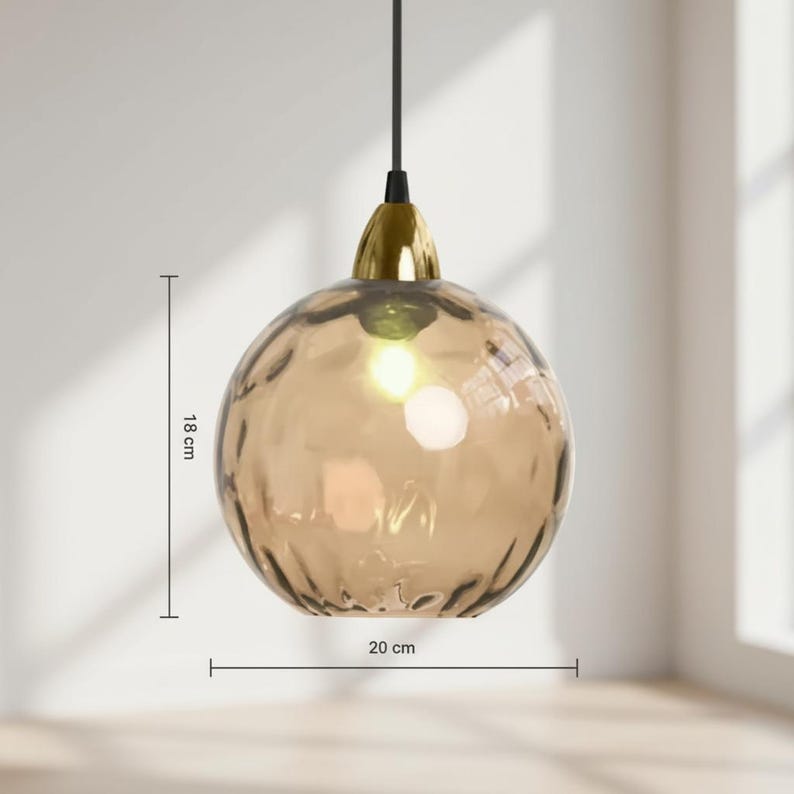 May include: A pendant light fixture with a textured, amber-colored glass globe, approximately 7 inches in diameter and 7 inches tall. The fixture has a gold-colored metal cap and a black cord. The light is turned on, illuminating the interior.