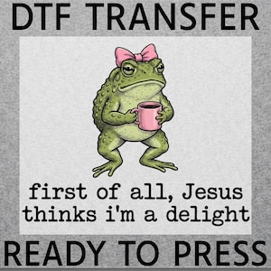 May include: A DTF transfer featuring a green toad wearing a pink bow and holding a pink mug. The text reads: DTF TRANSFER, first of all, Jesus thinks i'm a delight, READY TO PRESS. The design is on a light gray background with a dark gray border.