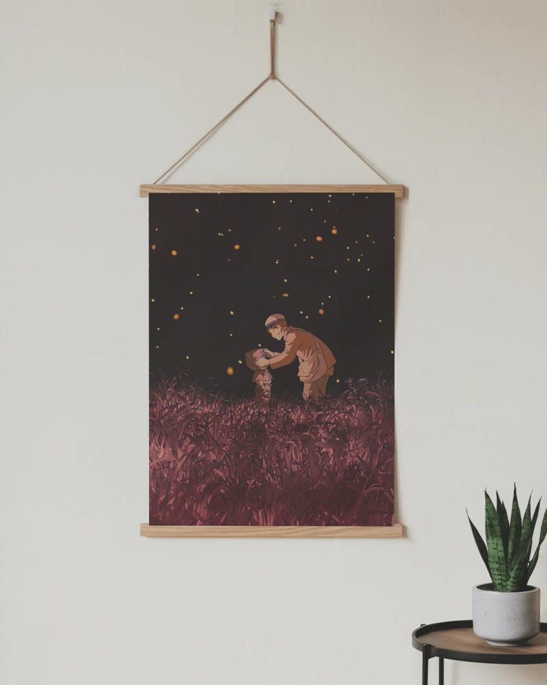 May include: A framed art print depicting a scene of two figures in a field at night, illuminated by glowing orbs. The print is mounted on wooden bars and suspended by a natural cord, creating a minimalist aesthetic. The artwork features warm tones and a dreamy atmosphere.
