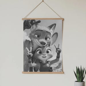 May include: A black and white wall hanging featuring a fox and a rabbit character making peace signs with their hands. The artwork is held by two light-colored wooden bars at the top and bottom, suspended by a thin string attached to the top bar.