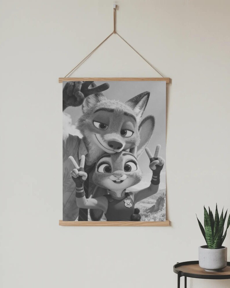 May include: A black and white wall hanging featuring a fox and a rabbit character making peace signs with their hands. The artwork is held by two light-colored wooden bars at the top and bottom, suspended by a thin string attached to the top bar.