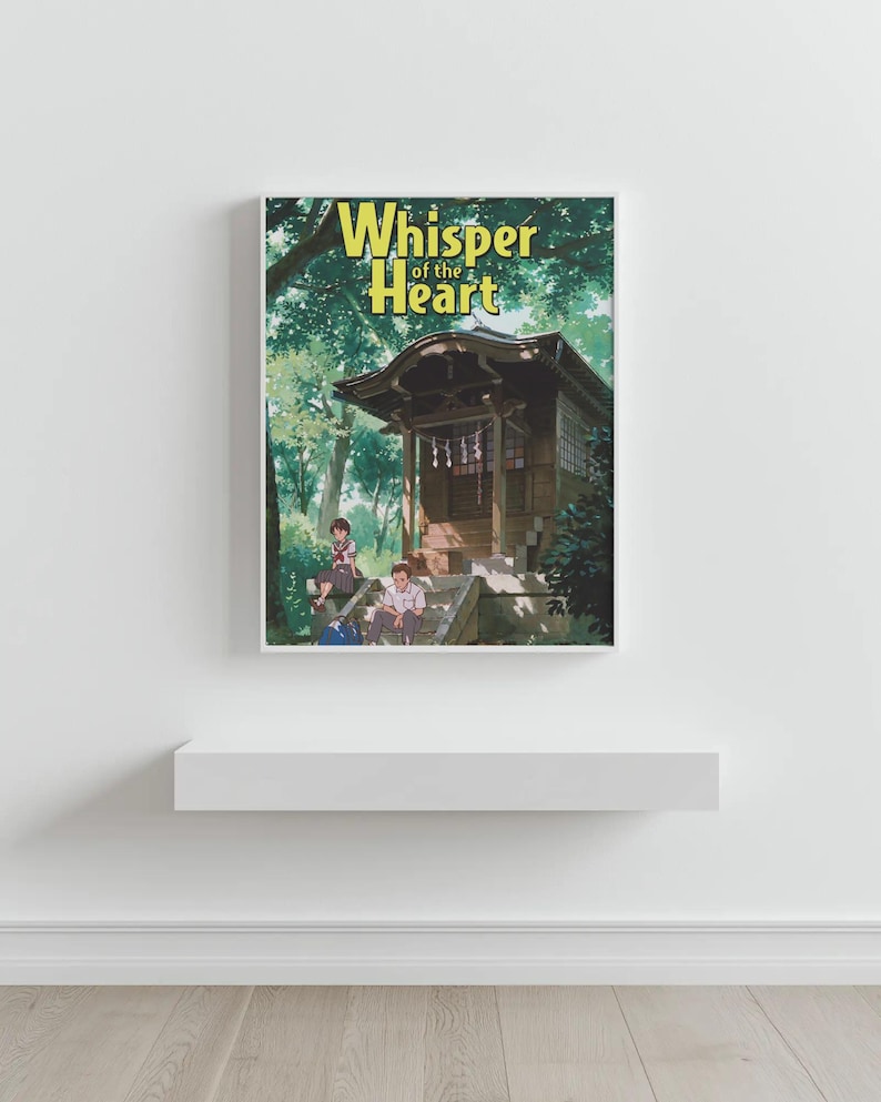 May include: A framed print with the title "Whisper of the Heart" in yellow. The image shows a traditional Japanese building with people in a green forest setting. The print is displayed on a white shelf, against a white wall.