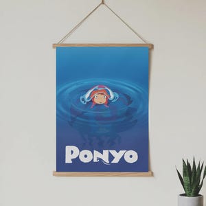 Pu&ograve; includere: Un poster con il personaggio animato Ponyo in una scena oceanica blu. Il poster ha una cornice in legno ed &egrave; sospeso da una corda. La parola "PONYO" &egrave; scritta in lettere bianche in grassetto nella parte inferiore del poster.