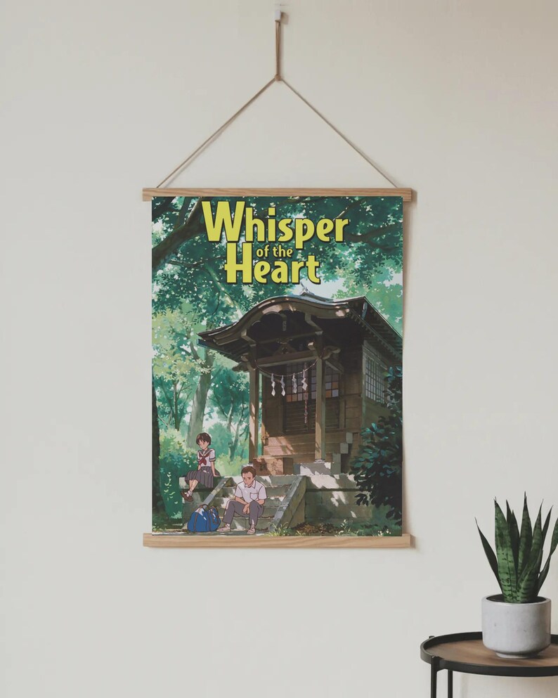 May include: A poster with the text "Whisper of the Heart" in yellow lettering, hanging from a wooden frame. The poster depicts an anime scene of a Japanese shrine with two people sitting on the steps.
