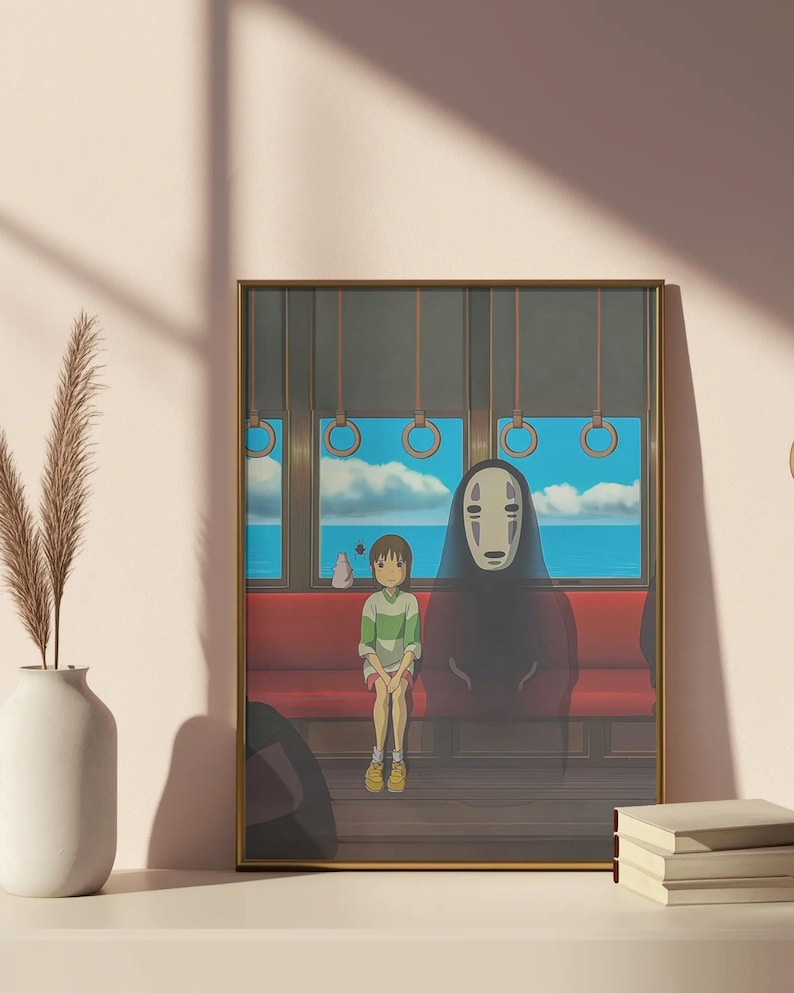 May include: Framed art print featuring a scene from an animated film. A young person in a green and white striped shirt sits on a red bench next to a tall, cloaked figure with a white mask. The background shows a seascape through train windows.