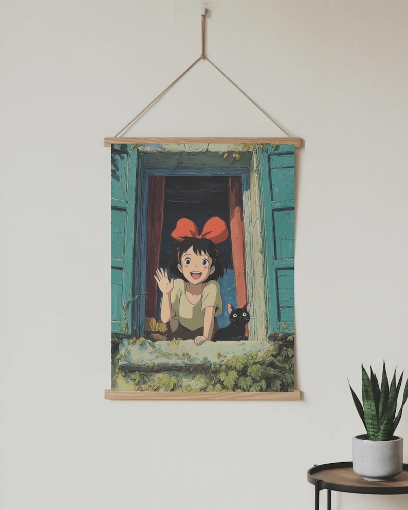 Puede incluir: Un tapiz de pared con una ilustraci&oacute;n de estilo anime. Una joven con un lazo rojo saluda desde una ventana, acompa&ntilde;ada por un gato negro. La ventana tiene contraventanas azules y vides verdes. La obra de arte est&aacute; suspendida por un marco de madera y una cuerda.