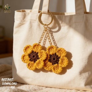 May include: A pair of crochet sunflower keychains with gold-colored chain and ring, hanging from a beige tote bag. The sunflowers have yellow petals and brown centers. The text "INSTANT DOWNLOAD PDF" is visible.