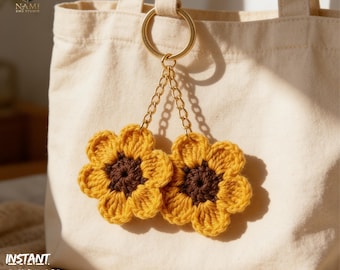 May include: A pair of crochet sunflower keychains with gold-colored chain and ring, hanging from a beige tote bag. The sunflowers have yellow petals and brown centers. The text "INSTANT DOWNLOAD PDF" is visible.