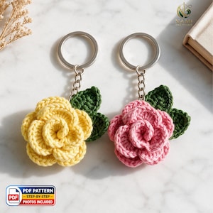 Op de afbeelding: Twee gehaakte bloemsleutelhangers, één geel en één roze, elk voorzien van donkergroene bladeren en een zilveren metalen ring. De afbeelding bevat een logo van Nami Emi Studio en een label voor een PDF-patroon met stap-voor-stap foto's.
