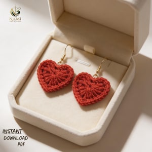 May include: A pair of red heart-shaped crochet earrings with gold-colored hooks, displayed in an open white jewelry box. The earrings are handmade and have a textured appearance. The image also includes the text "INSTANT DOWNLOAD PDF".