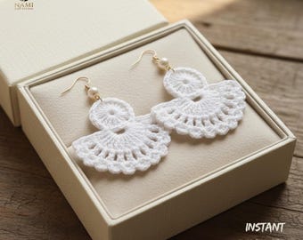 May include: White crochet earrings with a fan-like design, displayed in a cream-colored box. The earrings have a circular top and a scalloped bottom edge, with a small pearl accent. The box is open, revealing the earrings on a beige interior.