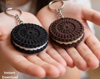 May include: Two round crochet cookie keychains with metal rings. One keychain features a black cookie with a white cream center, while the other is a brown cookie with a light green and white cream filling. Text reads NAMI EMB STUDIO.