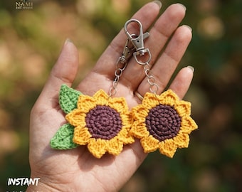 May include: Two crochet sunflower keychains with yellow petals and a dark purple center are displayed. Each keychain has a silver-colored clasp and chain. A green leaf is attached to one of the sunflowers. The text "INSTANT DOWNLOAD PDF" is visible.