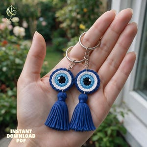 May include: Two matching crochet keychains featuring a circular evil eye motif in concentric rings of dark blue, white, light blue, and black. Each keychain is attached to a silver metal split ring and includes a dark blue thread tassel.