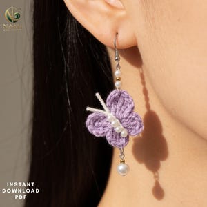 May include: A dangle earring featuring a crocheted lavender butterfly with white thread antennae. The butterfly body is accented with a vertical row of four small white beads. A silver-toned hook connects to a chain with two small white beads.