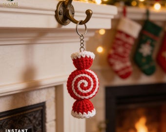 May include: A crocheted candy-shaped keychain featuring a central red and white spiral pattern with red and white textured ends. The ornament is attached to a silver-toned metal split ring and chain, hanging from a metal hook against a fireplace.