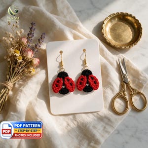 May include: A pair of handmade crochet ladybug earrings featuring red and black yarn bodies with gold-toned metal fishhook ear wires. The ladybugs have circular black centers with red wings accented by small black stitched dots, displayed on a white card.