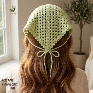 May include: A light green, crocheted head covering with a square shape and a bow tie in the back. The text "INSTANT DOWNLOAD PDF" is visible in the lower left corner. The head covering is made of a light green yarn.